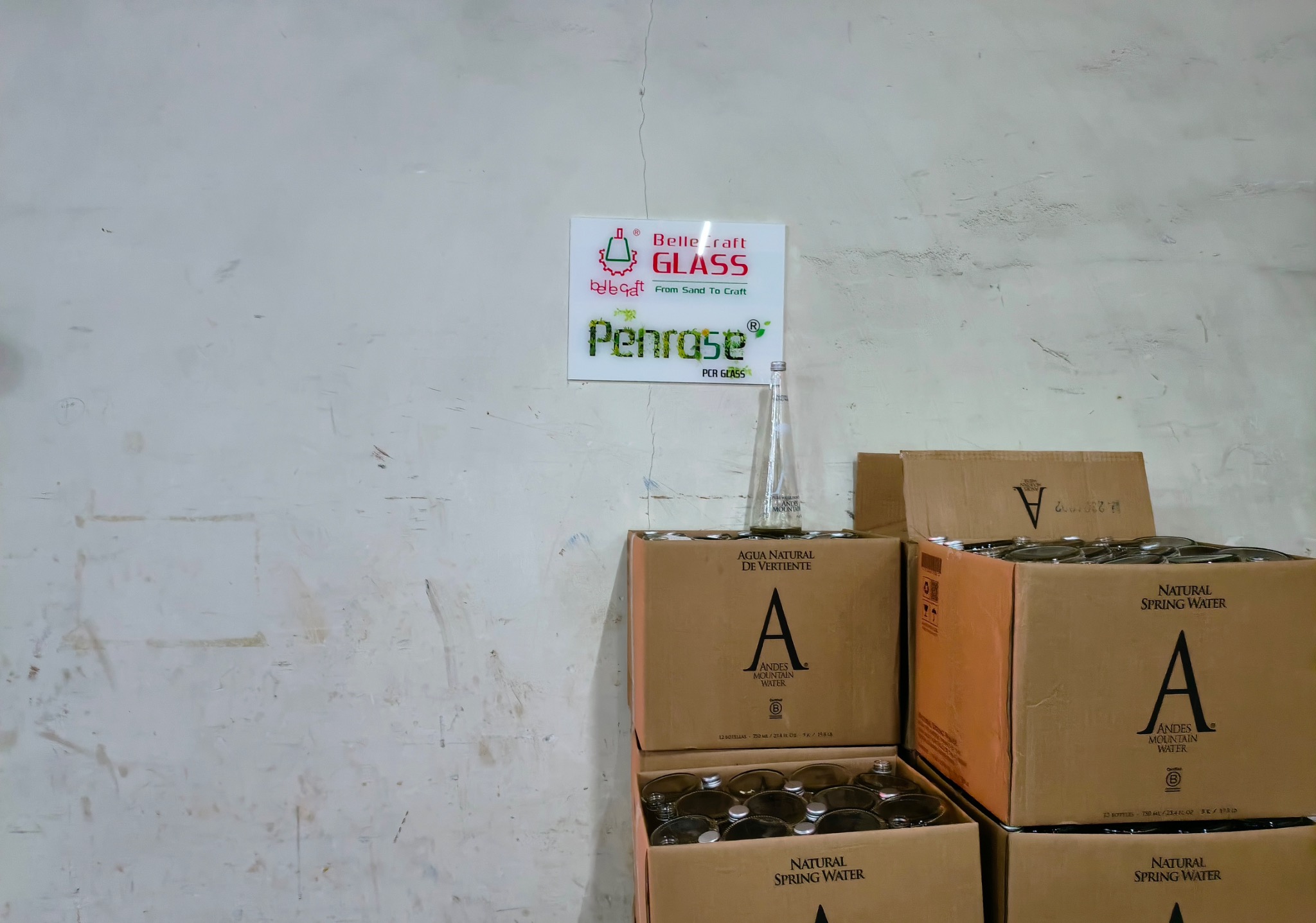 Used glass water bottles gathered in cartons beneath a BelleCraft and Penro5e sign